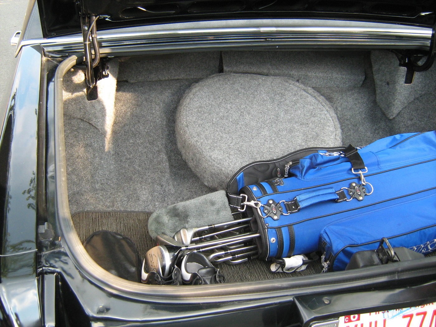 An open Cadillac trunk contains a blue golf bag and clubs with unused space beside it