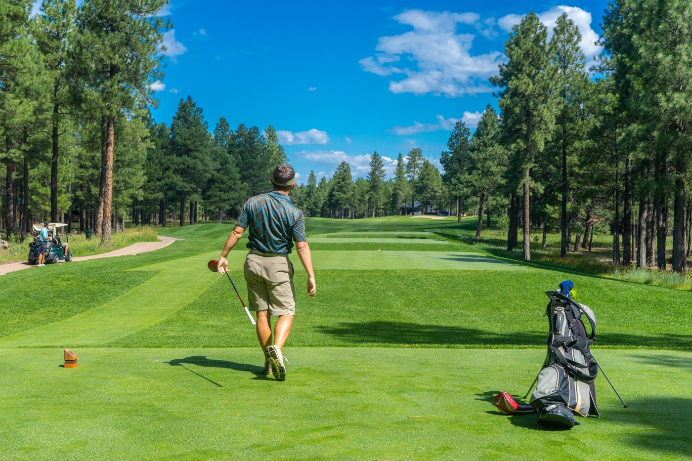 A golfer walks across a tee with a stand bag nearby on the course
